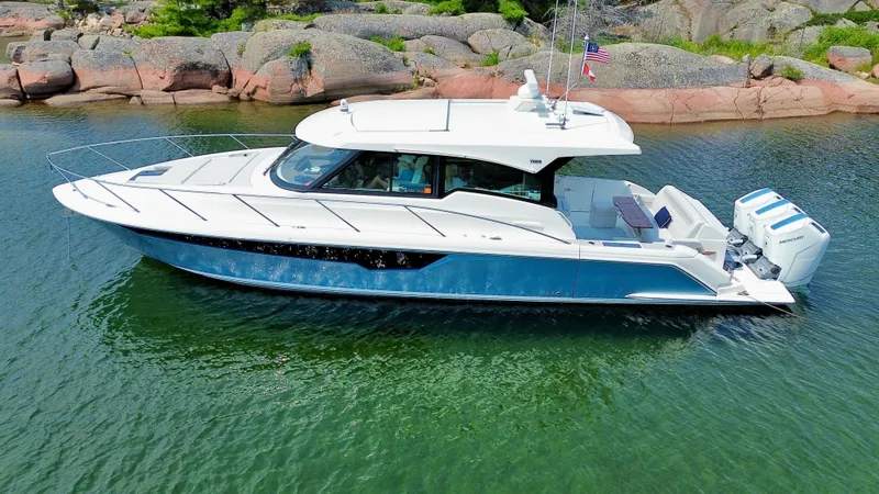 Slide: The Image of 2025 Tiara Yachts 48 LE on calm water, surrounded by rocks and trees. - 7