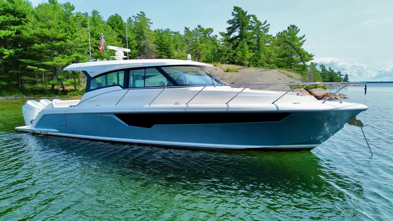 The Image of 2025 Tiara Yachts 48 LE on calm water near a wooded shoreline. - 0