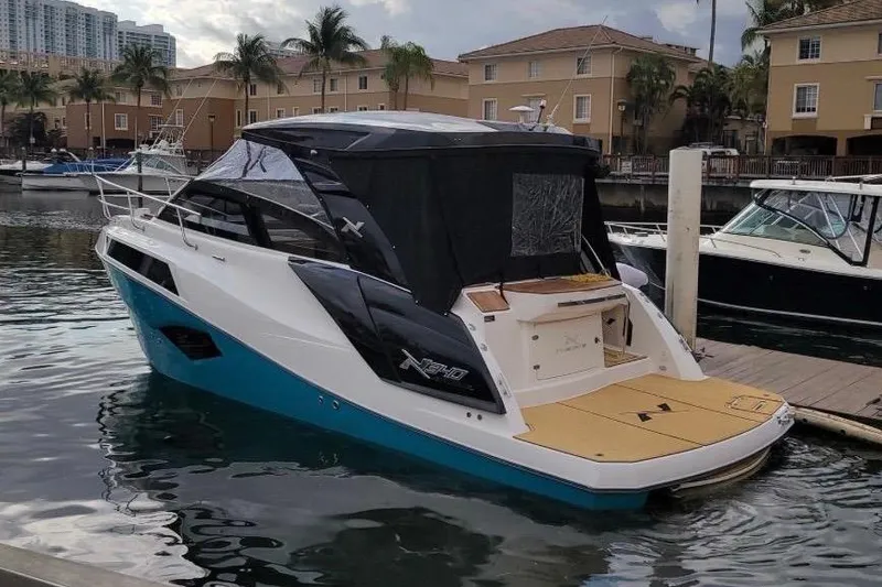 Slide: The Image of A 2023 NX Boats 340 Sport Coupe docked at a marina, surrounded by buildings and palm trees. - 5