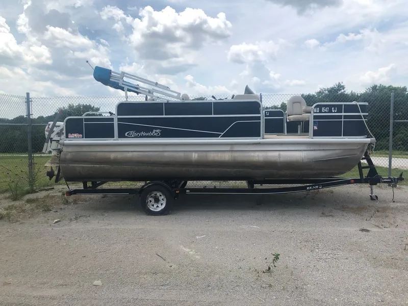 Slide: The Image of A 2018 Misty Harbor A-1885CF pontoon boat on a trailer in front of a fence. - 1