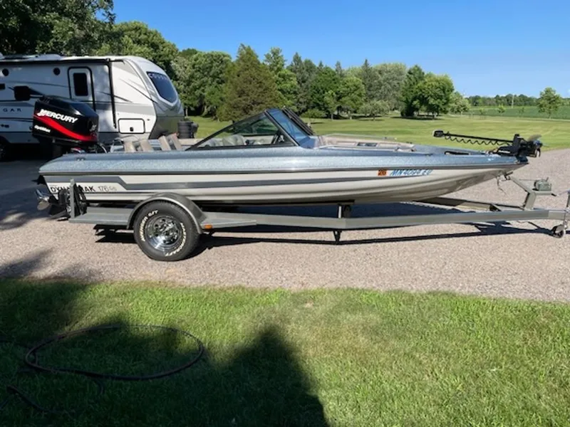 The Image of A 1984 Ebbtide Dyna-Trak boat on a trailer, parked on a road next to an RV. - 0