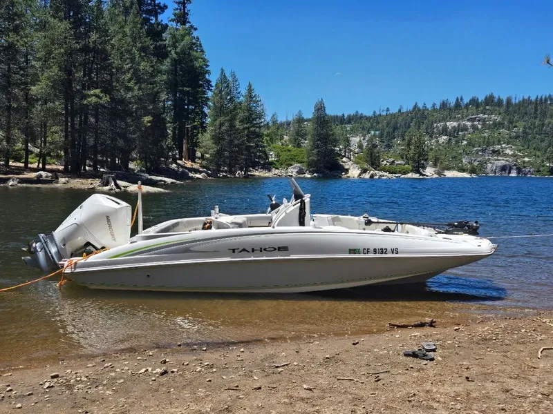 The Image of A 2018 Tahoe 2150 CC boat is beached on a lake shore, surrounded by trees. - 0