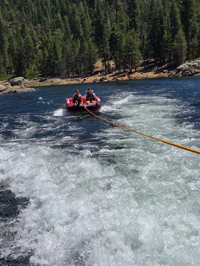 Slide: The Image of Two people being towed on an inflatable tube behind a boat, surrounded by forest and water. - 10