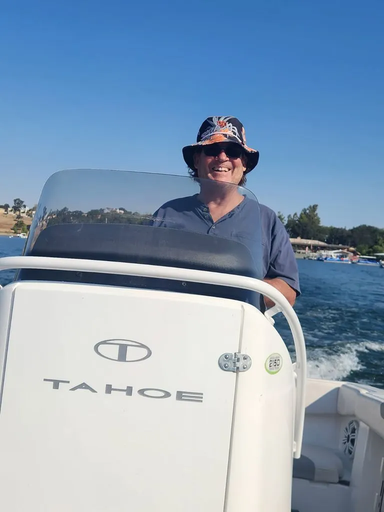 Slide: The Image of A man is steering a 2018 Tahoe 2150 CC boat on sunny waters. - 9