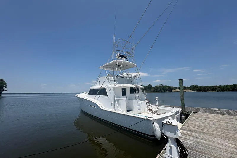 The Image of 1973 Hatteras 53 Convertible yacht docked on a serene lake under a clear blue sky. - 1