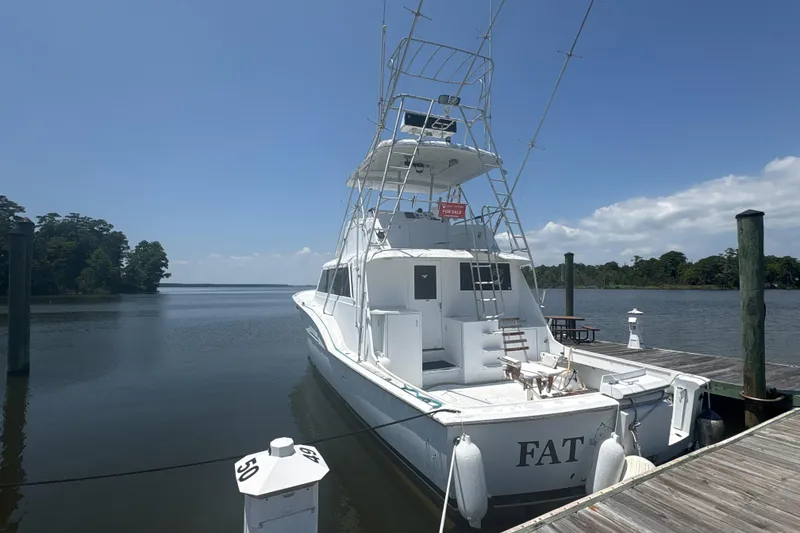 Slide: The Image of 1973 Hatteras 53 Convertible yacht docked, for sale sign visible, clear sky background. - 2