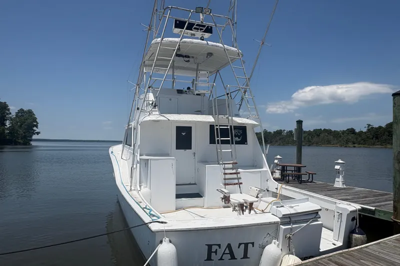 Slide: The Image of 1973 Hatteras 53 Convertible yacht docked by a serene lake under a clear blue sky. - 92
