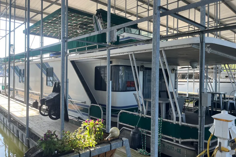 Slide: The Image of 1997 Lakeview 65x18 houseboat docked, featuring green canopy and outdoor seating area. - 3