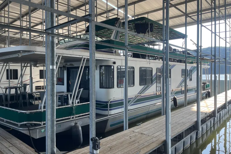 Slide: The Image of 1997 Lakeview 65x18 houseboat docked in a marina, featuring green accents and spacious deck. - 2