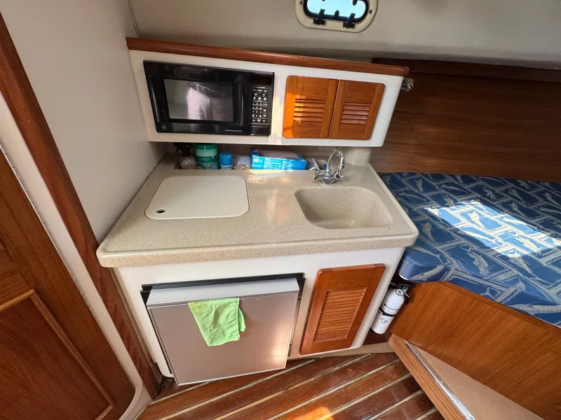 Slide: The Image of Compact boat galley with sink, microwave, and fridge, next to a cushioned berth. - 29