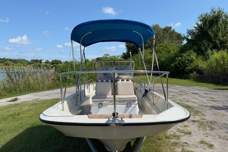 Slide: The Image of 1987 Boston Whaler 17 Montauk boat with blue canopy, parked on grassy area. - 14