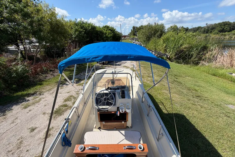 Slide: The Image of 1987 Boston Whaler 17 Montauk boat with blue canopy, parked on grassy area under clear sky. - 10