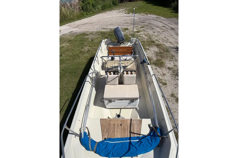 Slide: The Image of 1987 Boston Whaler 17 Montauk boat interior with seating and motor, parked on grass. - 5