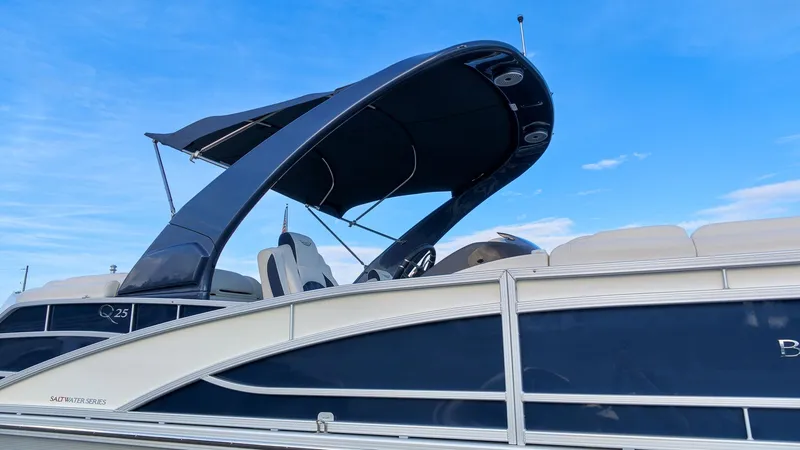 The Image of A sleek 2024 Bennington 25 QFBA pontoon boat with a blue hull and curved bimini top. - 1
