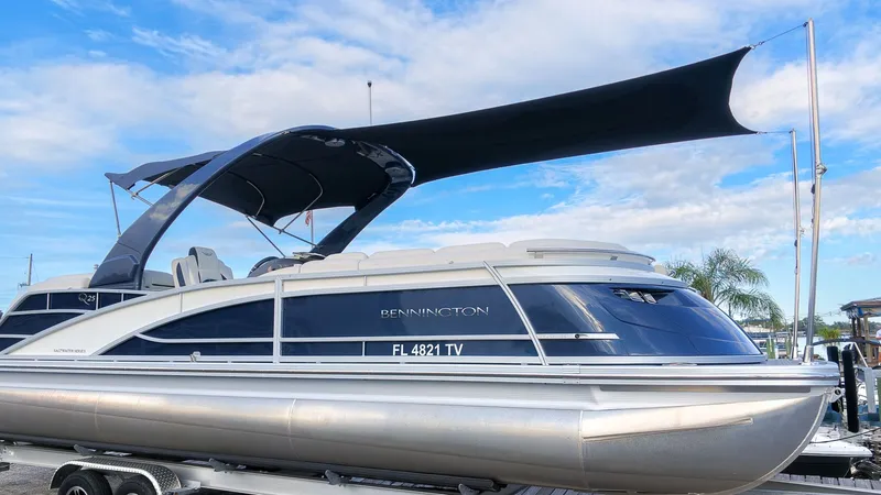 Slide: The Image of A sleek 2024 Bennington 25 QFBA pontoon boat with a black sunshade, on a trailer. - 2