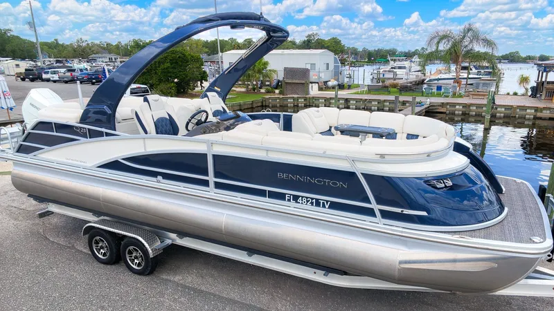 Slide: The Image of A sleek 2024 Bennington 25 QFBA pontoon boat on a trailer, set against a scenic harbor. - 26