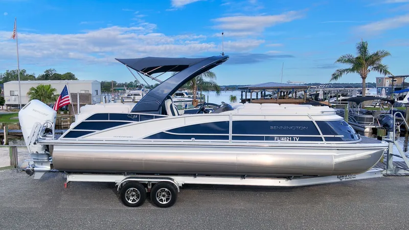 Slide: The Image of A sleek 2024 Bennington 25 QFBA pontoon boat on a trailer, with a blue sky backdrop. - 25
