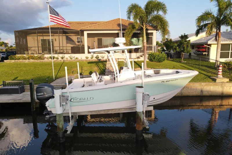 Slide: The Image of 2021 Robalo R230 Center Console boat docked by waterfront home with American flag. - 2