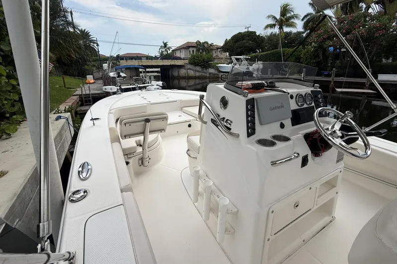 Slide: The Image of 2016 Robalo 246 Cayman boat interior with steering console and seating, docked near lush greenery. - 24