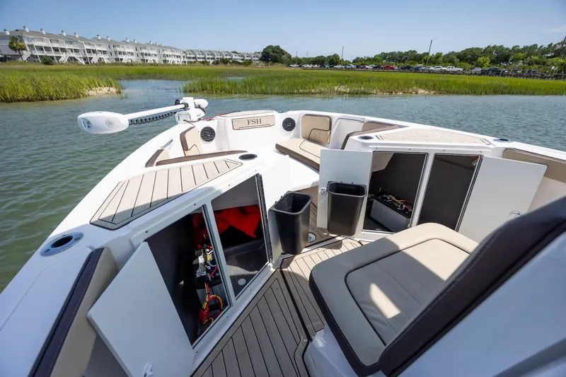 Slide: The Image of 2023 Yamaha Boats 222 FSH Sport E interior with open storage compartments on a calm waterway. - 15