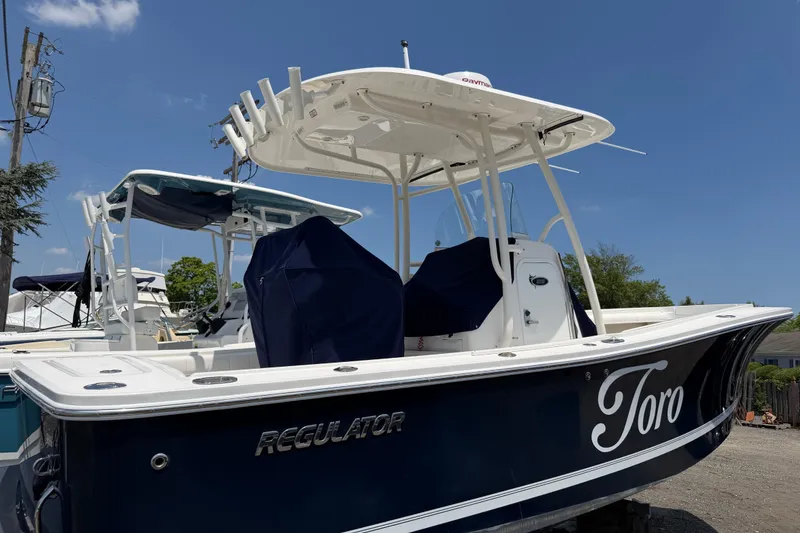 Slide: The Image of 2015 Regulator 23 Center Console boat with blue hull, docked under clear sky. - 2