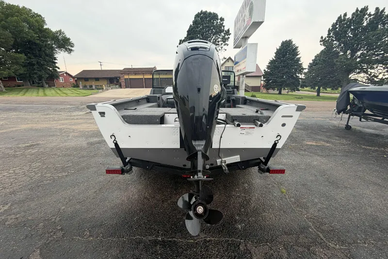 Slide: The Image of 2025 Lund 1775 Impact XS Sport boat, rear view with outboard motor, parked outdoors. - 2