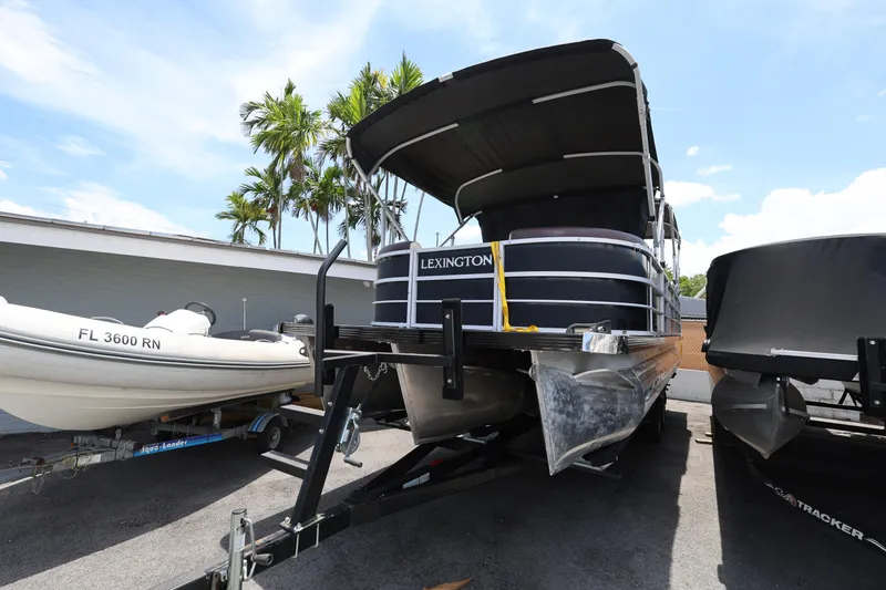 Slide: The Image of 2021 Lexington 525 Series 5 pontoon boat on trailer, parked outdoors under clear sky. - 7