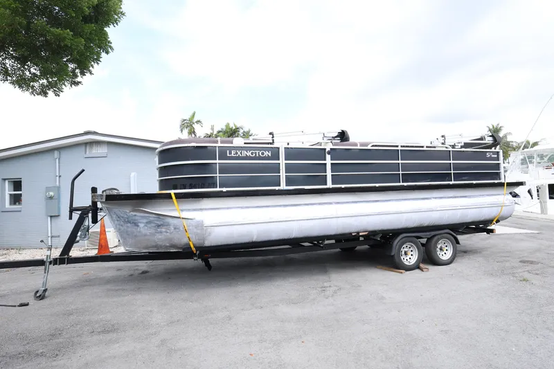The Image of 2021 Lexington 525 Series 5 pontoon boat on trailer, parked near a building. - 1