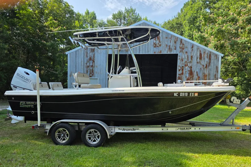 The Image of 2021 Carolina Skiff 21 Ultra Elite boat on trailer, parked near rustic barn. - 1