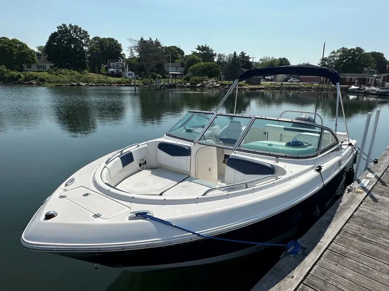 Slide: The Image of A 2018 Robalo R227 Dual Console boat docked at a calm pier with wooded shoreline in the background. - 5