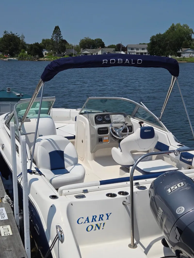 Slide: The Image of A 2018 Robalo R227 Dual Console boat docked. It features a blue bimini top and an outboard motor. - 32