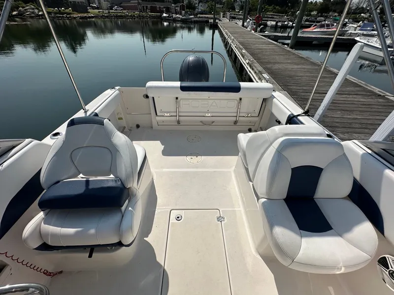 Slide: The Image of The image shows the cockpit of a 2018 Robalo R227 Dual Console boat. It features two cushioned seats and is docked in a calm marina. - 13