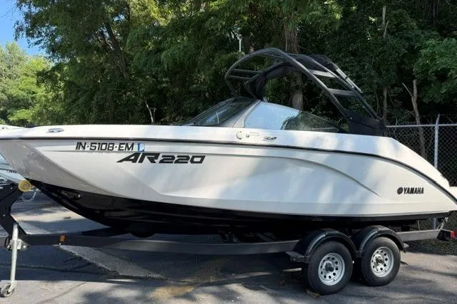 The Image of 2023 Yamaha Boats AR220 on trailer, parked outdoors with trees in background. - 0