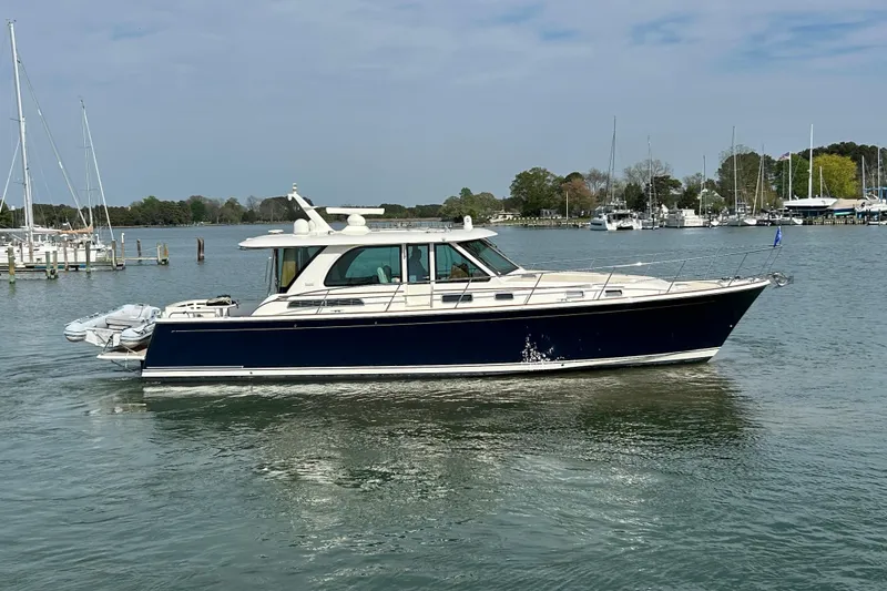 Slide: The Image of 2022 Sabre 45 Salon Express yacht cruising on a calm lake with marina backdrop. - 60