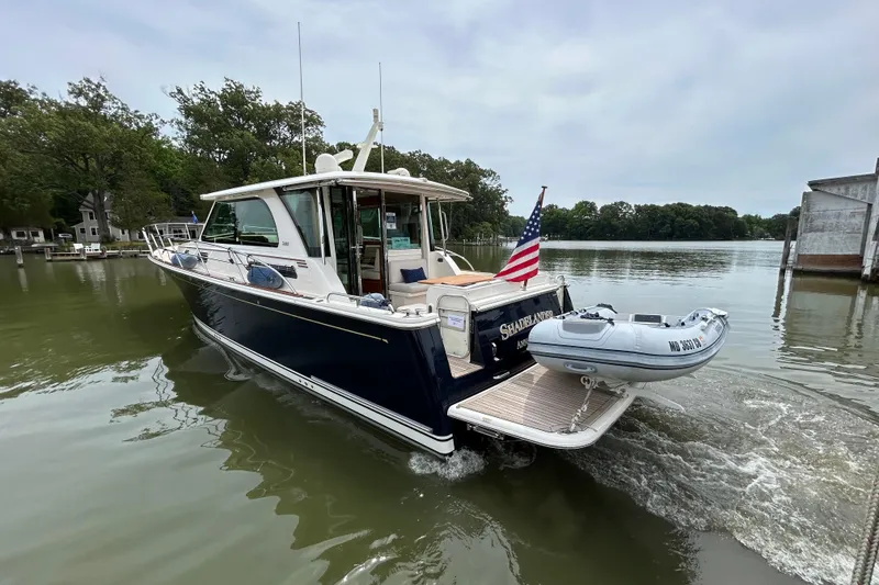 Slide: The Image of 2022 Sabre 45 Salon Express yacht cruising on a calm river with a small dinghy attached. - 61