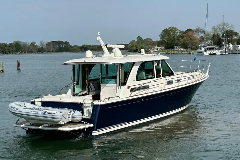 The Image of 2022 Sabre 45 Salon Express yacht cruising on a calm lake with a small dinghy attached. - 0