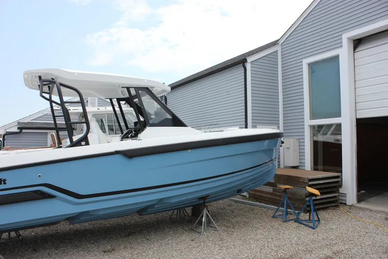 Slide: The Image of 2027 Wellcraft 28 T-Top boat in a marina, blue hull, parked on gravel. - 5
