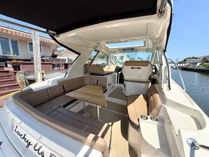 Slide: The Image of The image shows the cockpit of a 2017 Sea Ray Sundancer 350 Coupe. It features U-shaped seating with a wooden table, docked at a pier. - 6