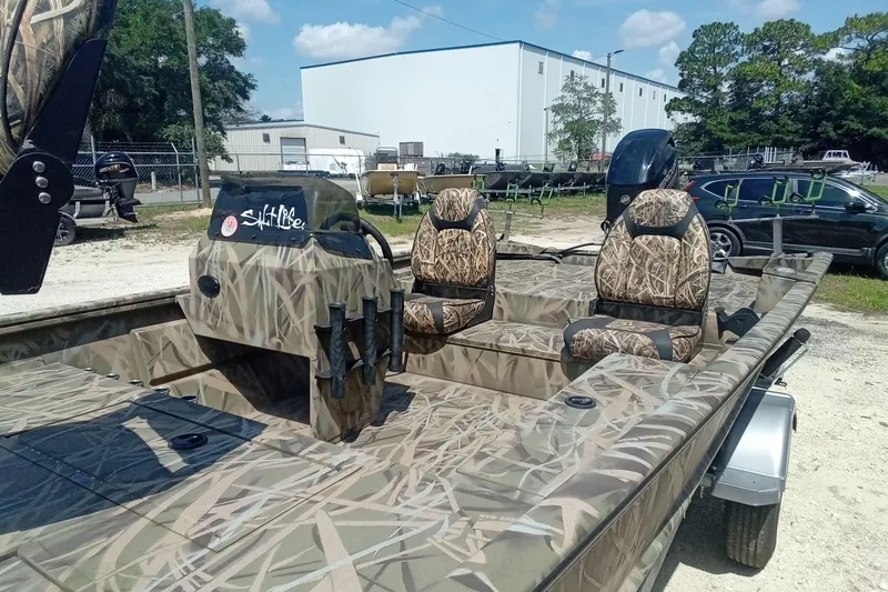 Slide: The Image of 2025 Lund 1760 Predator SC boat with camouflage design and seating, parked outdoors. - 27