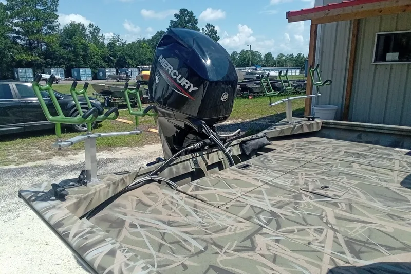 Slide: The Image of 2025 Lund 1760 Predator SC boat with Mercury engine and camouflage design, parked outdoors. - 17