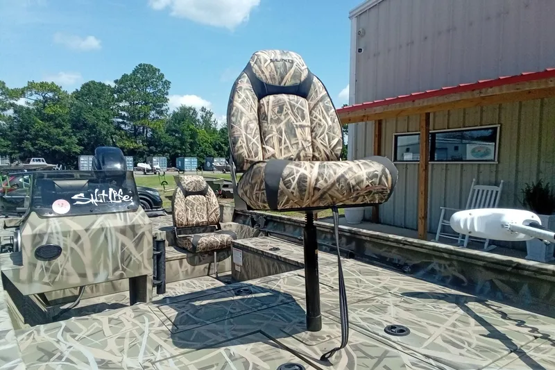 Slide: The Image of 2025 Lund 1760 Predator SC boat with camo seats, parked outdoors near a building. - 12