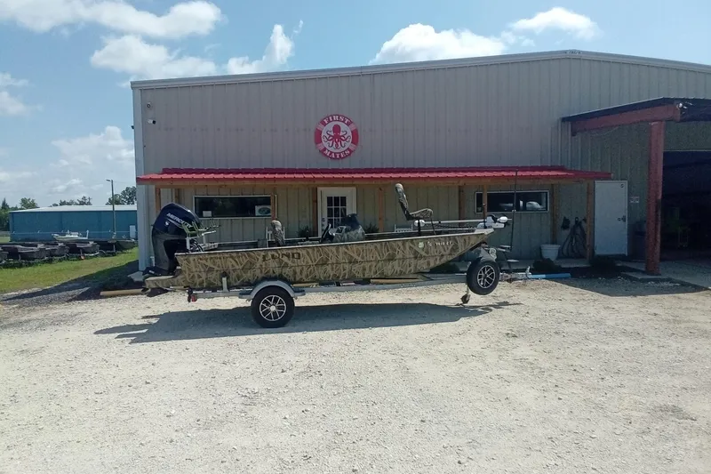 Slide: The Image of 2025 Lund 1760 Predator SC boat on trailer outside a metal building under a clear sky. - 6