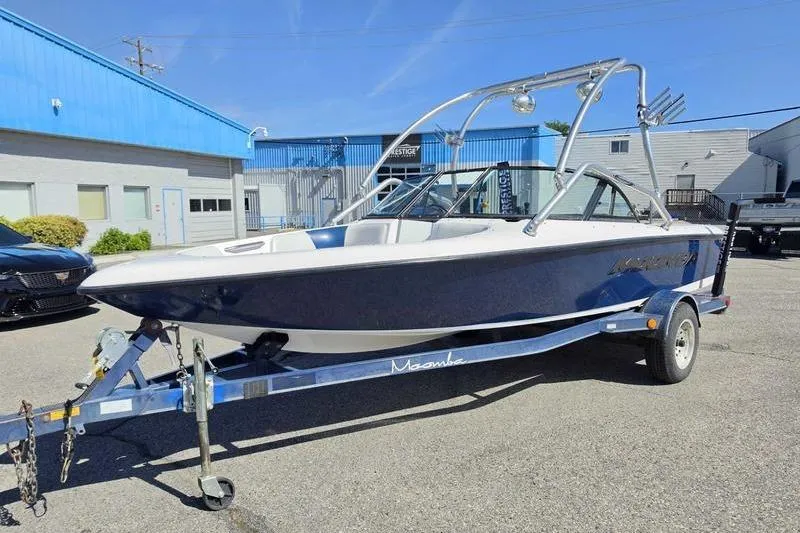 Slide: The Image of 1998 Moomba Outback boat on trailer, parked outdoors near blue building. - 2