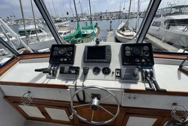 Slide: The Image of 1977 Californian 38 Motor Yacht helm with navigation instruments, overlooking marina with docked boats. - 46