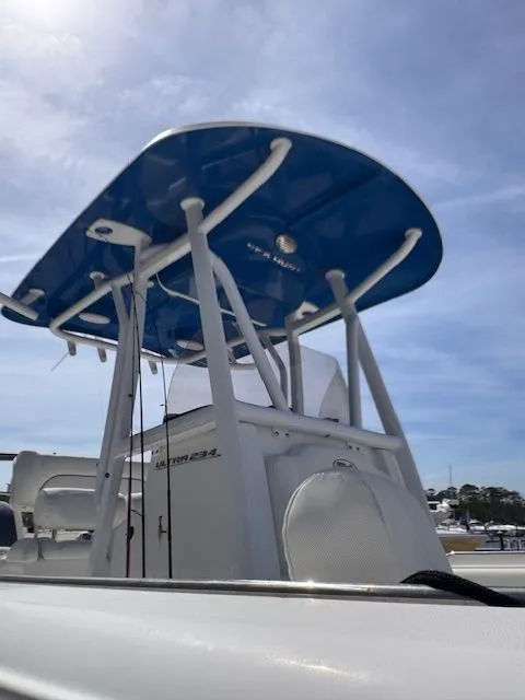 Slide: The Image of A Sea Hunt 234 SXS boat with a blue T-top and white hull, docked at a marina. - 12