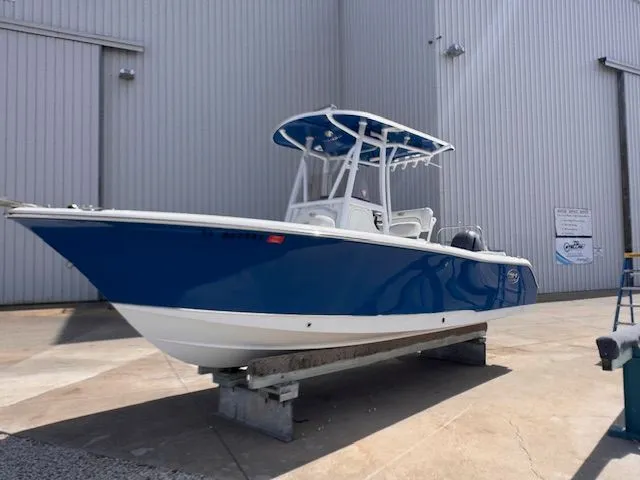 The Image of A blue and white Sea Hunt 234 SXS boat is on a dry dock outside a building. - 0