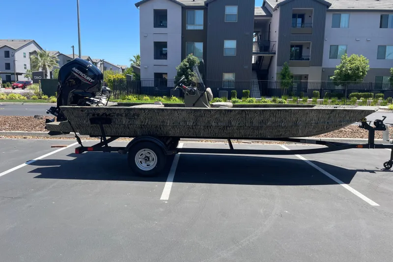 Slide: The Image of 2026 Tracker Grizzly 1860 CC boat on trailer in parking lot, residential buildings in background. - 16
