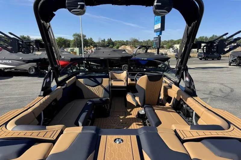 Slide: The Image of 2026 MasterCraft XT23 boat interior with tan and black seating, parked outdoors. - 7
