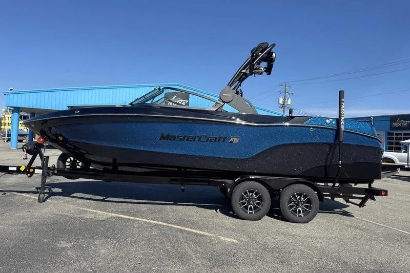 The Image of 2026 MasterCraft XT23 boat on trailer, parked outdoors near blue building. - 0