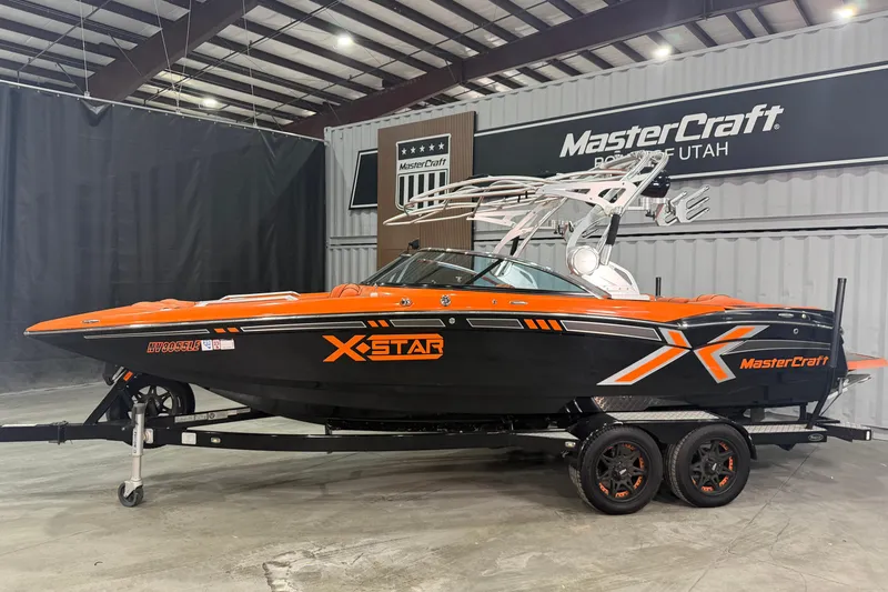 Slide: The Image of 2013 MasterCraft XStar boat in showroom, orange and black design, on trailer. - 2